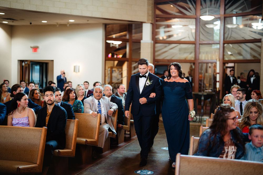 A wedding processional in a church as attendants walk down the aisle lined with wooden pews.