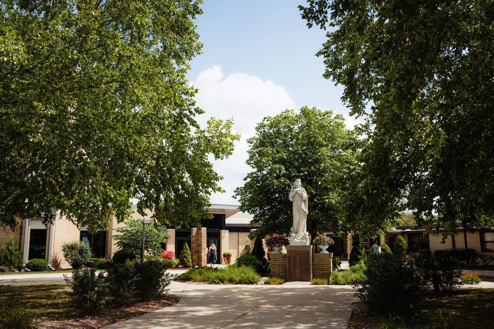 White stone statue in courtyard surrounded by lush green trees on sunny day.