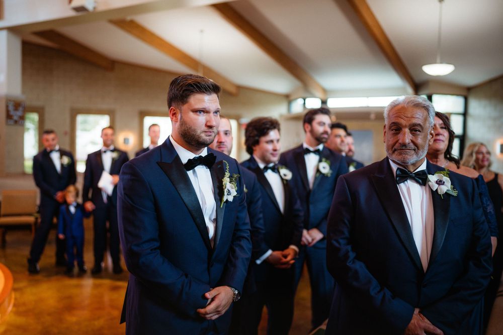 Wedding attendees in formal black tie attire gathered in church sanctuary.