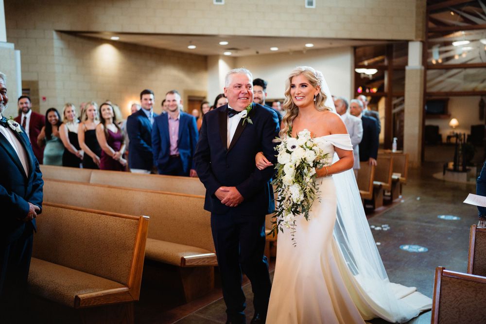 Processional moment in church with cascading bridal bouquet and formal attire.