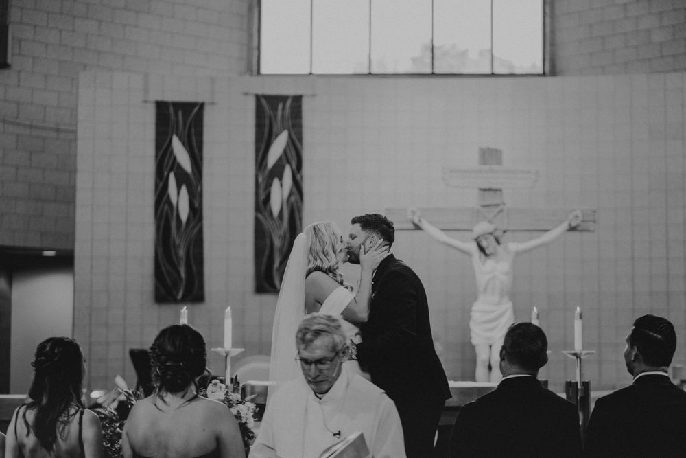Black and white photo of wedding ceremony in church with crucifix on wall.