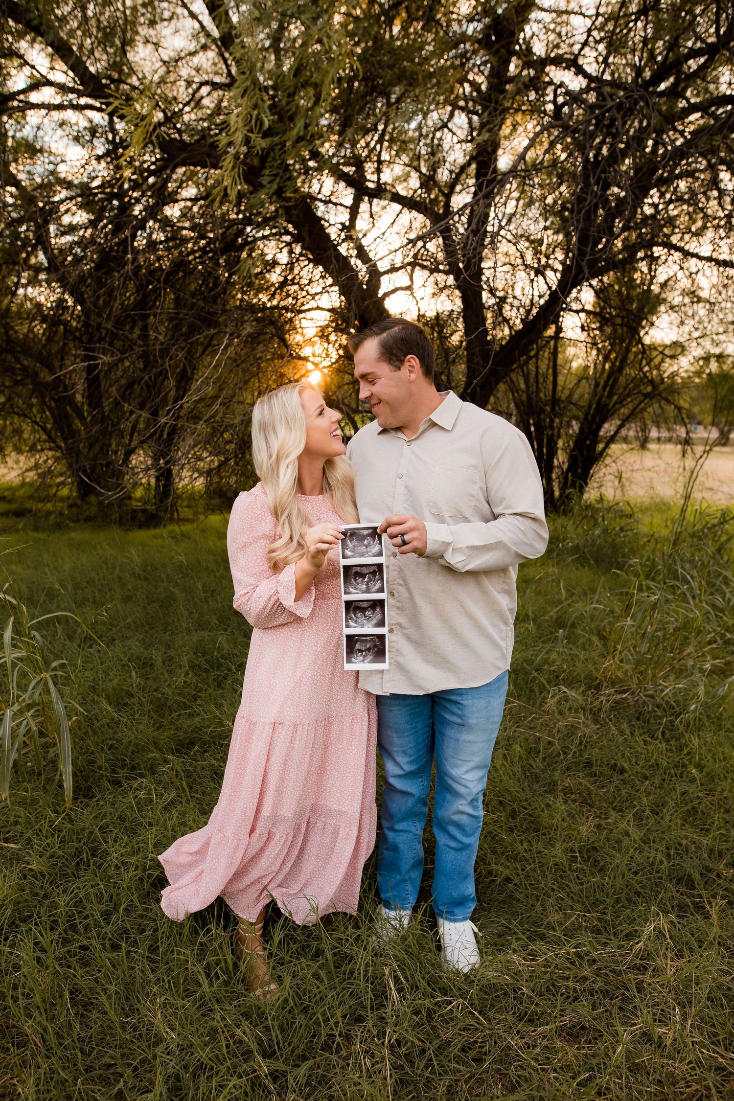 This couple is holding their ultrasound for an announcement portrait in a beautiful green field.