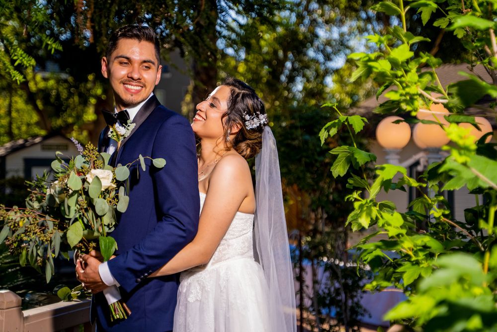 A wedding couple poses together in a lush garden setting with bright greenery and natural sunlight.