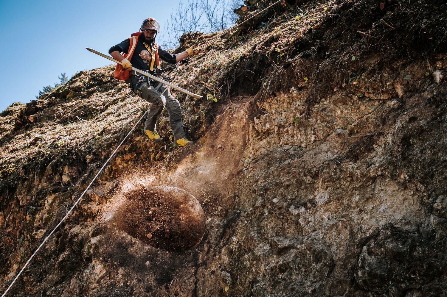 A person works on a mining or construction project on a rocky cliff face with dirt spraying in action shot.