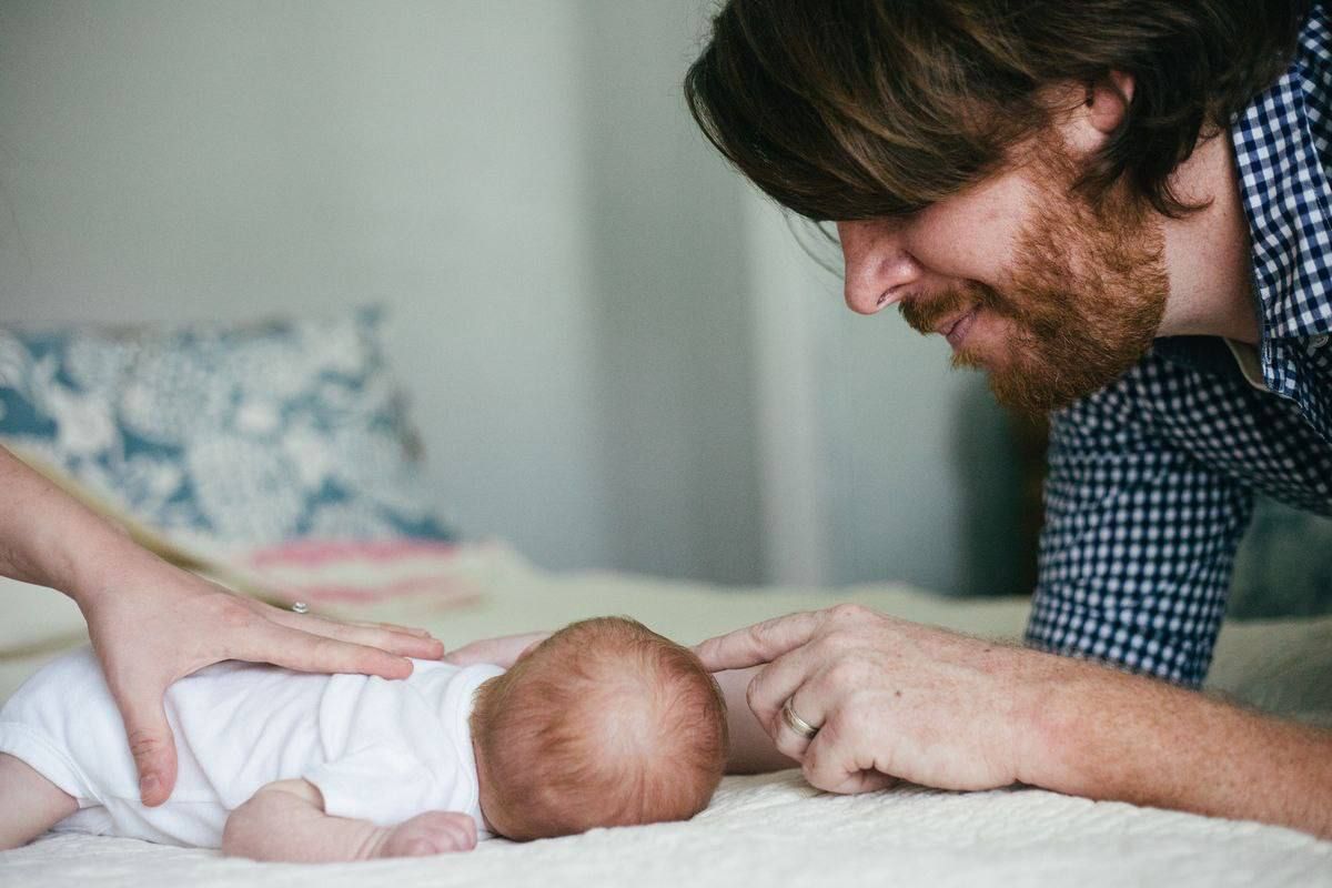 An intimate moment between parent and newborn on white bedding in soft natural light.