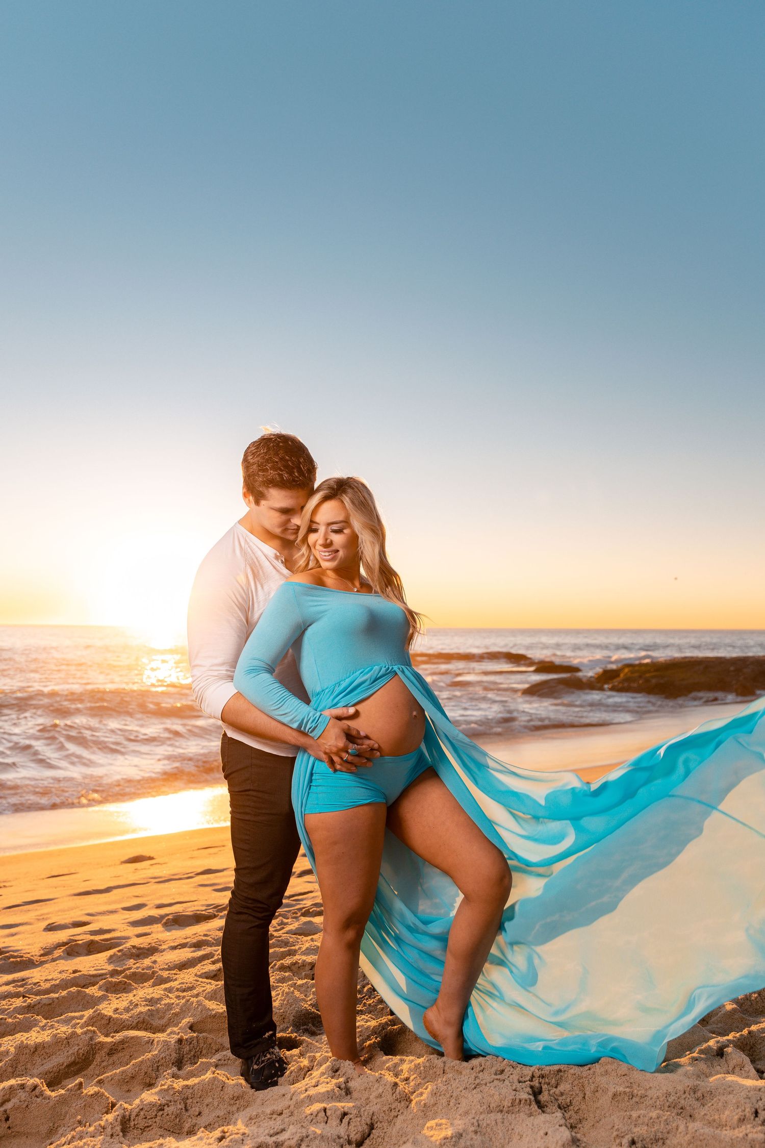 Intimate maternity beach photo with flowing turquoise dress during golden hour.