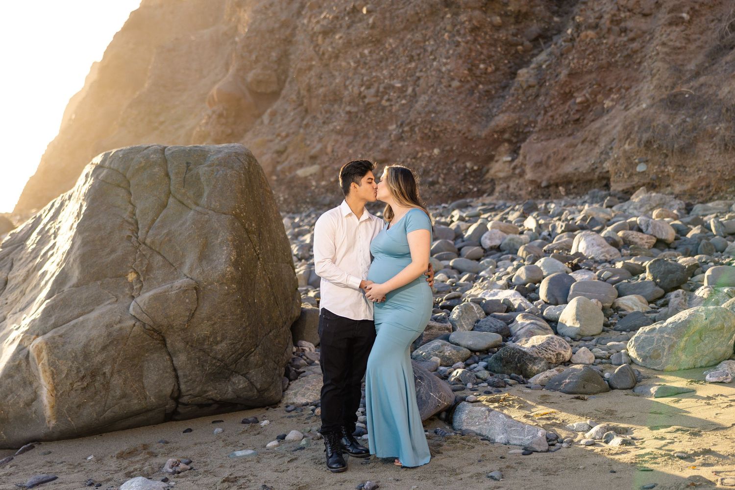 Romantic couple posing against rocky beach cliff in sunset light.