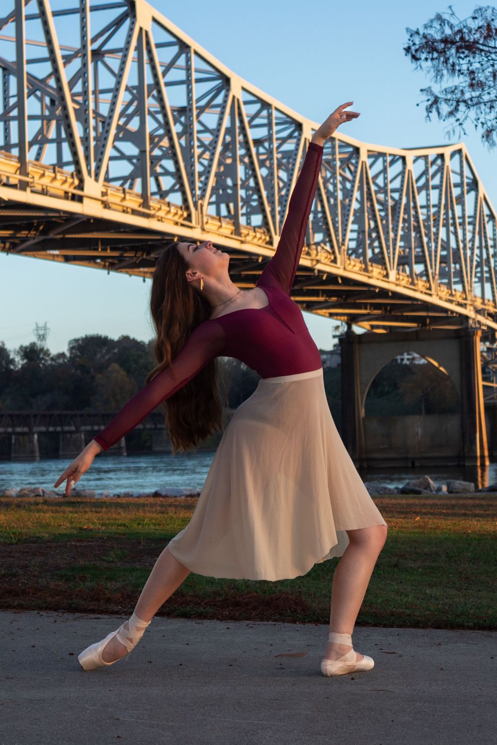 A ballet dancer performs graceful movements in front of a golden bridge at sunset, creating an artistic silhouette.