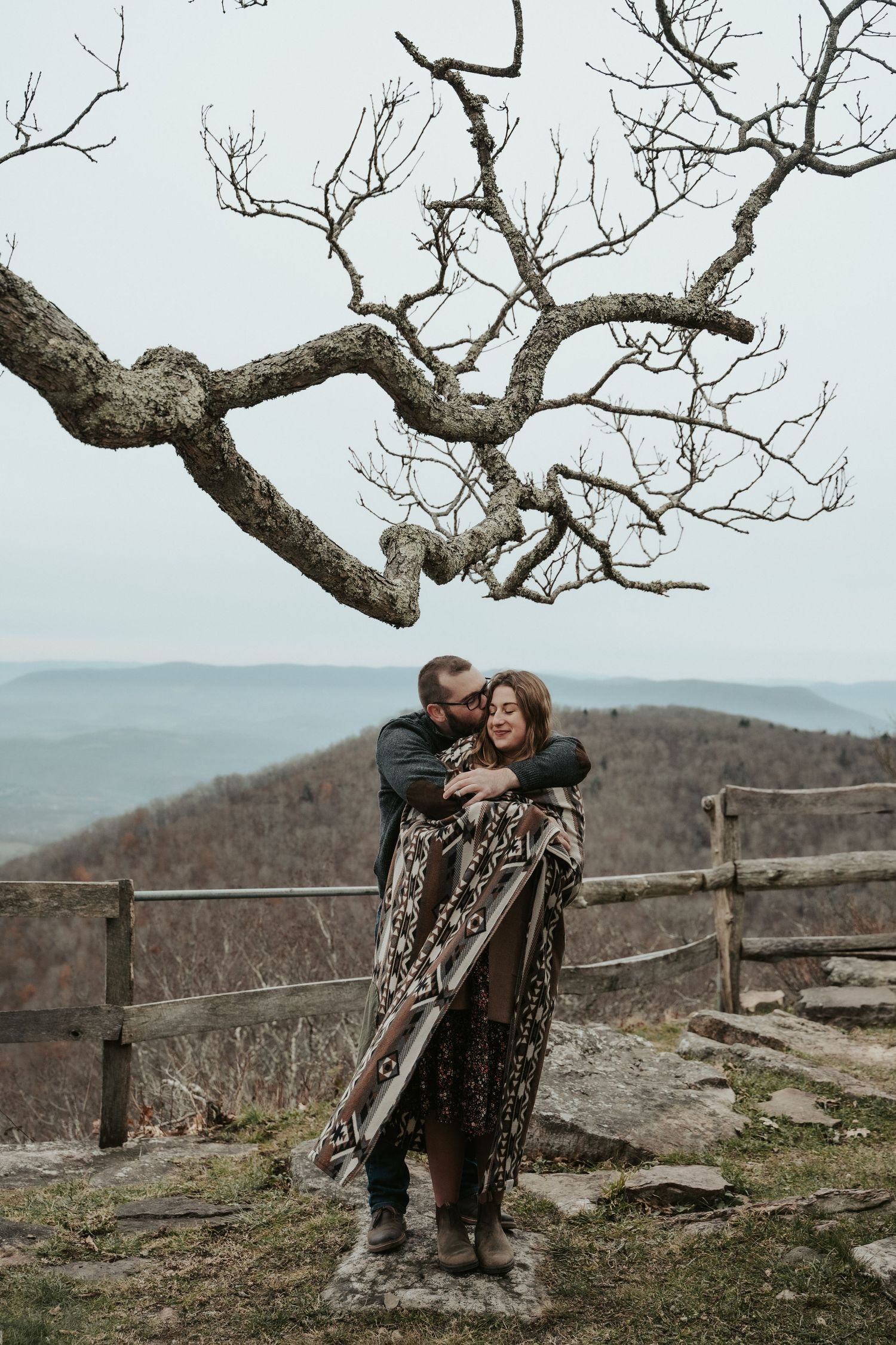 A couple in Shenandoah, Virginia wrapped in each others arms on a mountain in a blanket for an intimate engagement shoot
