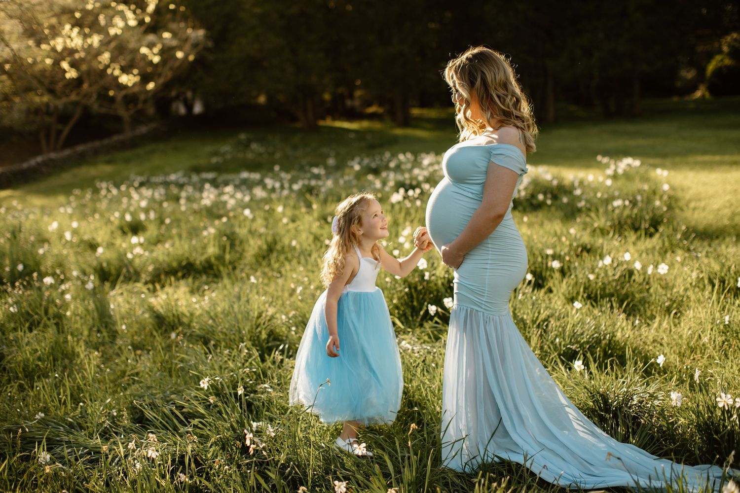 Two people in light blue dresses sit together in sunlit meadow during golden hour.