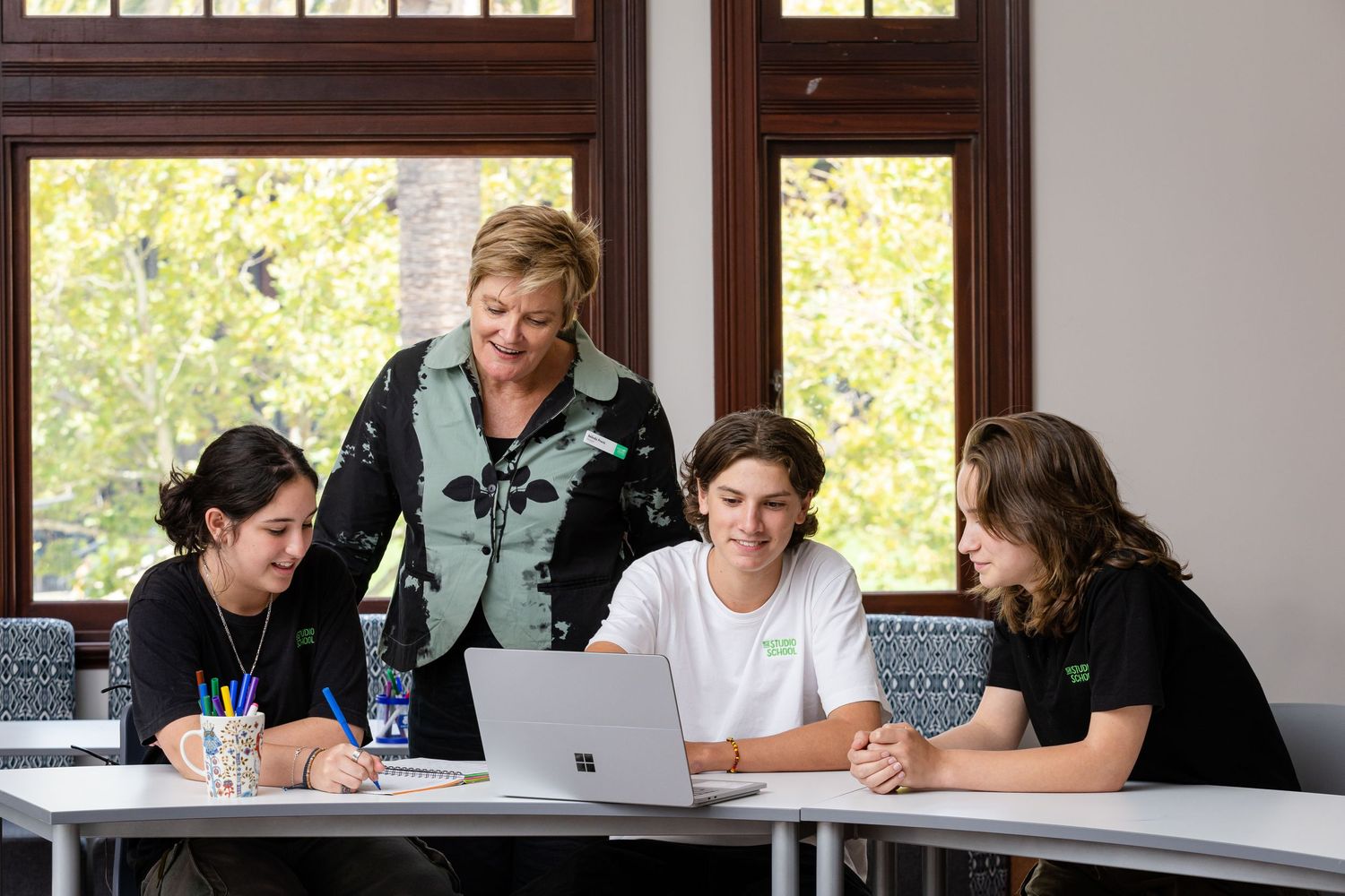 Students gather around a laptop for a study session in a bright classroom.