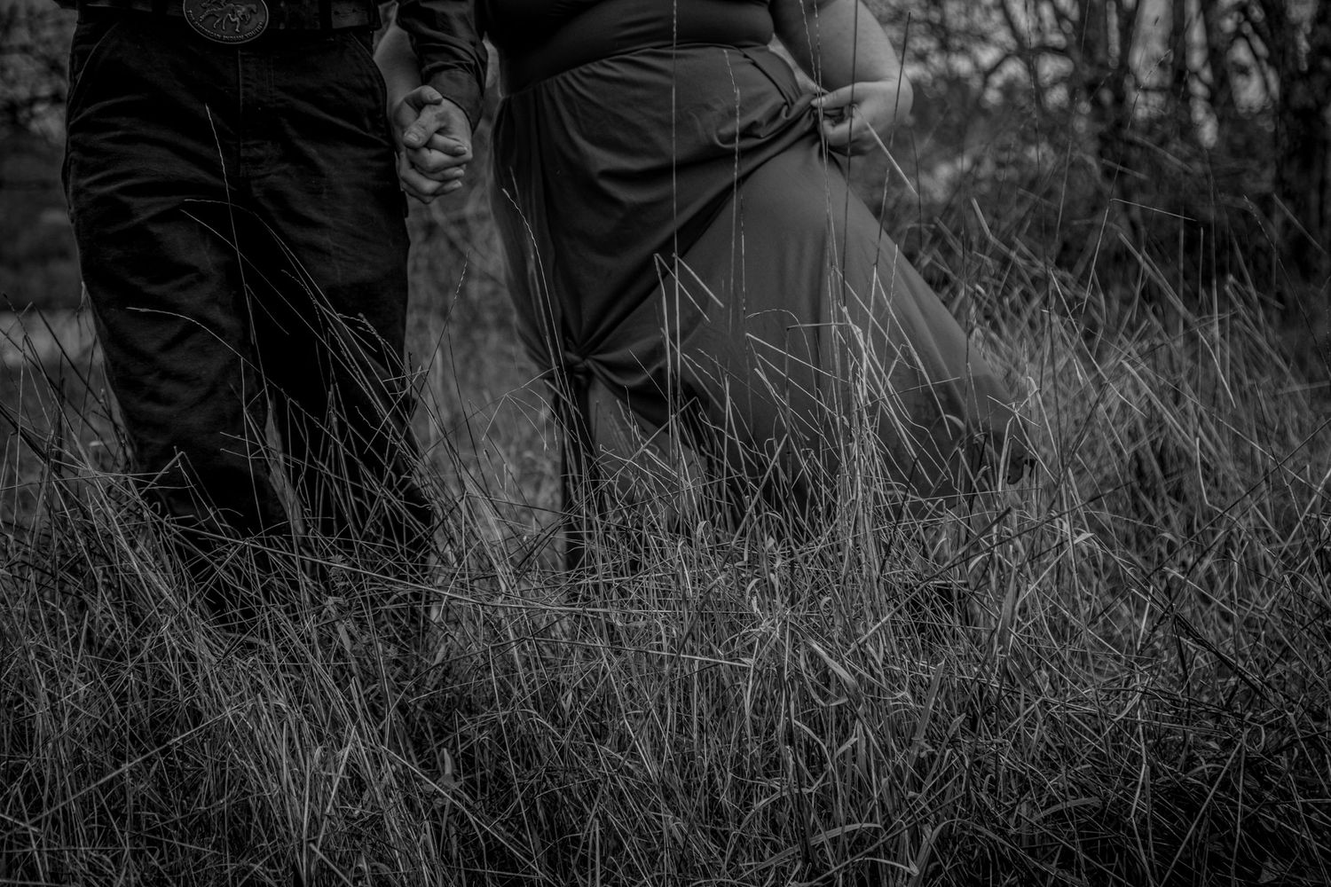 Black and white artistic detail shot of people's legs in tall grass.