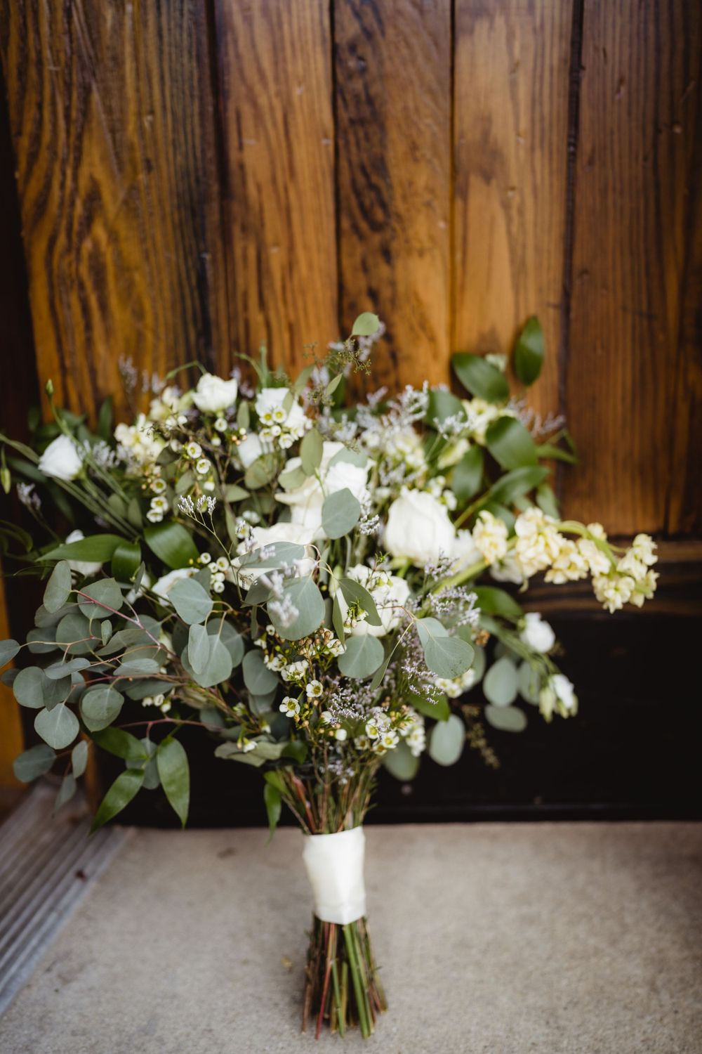 Elegant white and green wedding bouquet with eucalyptus leaves against wooden background.