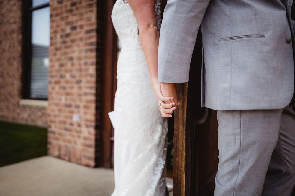 Close-up of wedding couple holding hands against brick building exterior.