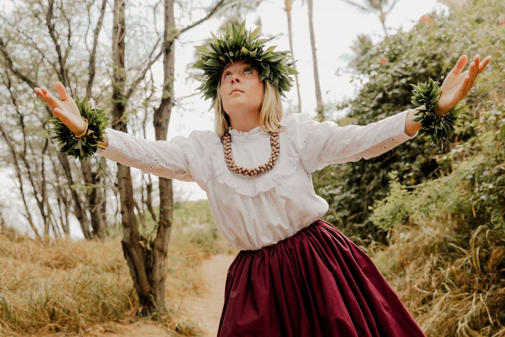 Expressive hula performance in forest setting with traditional costume and lei adornments.
