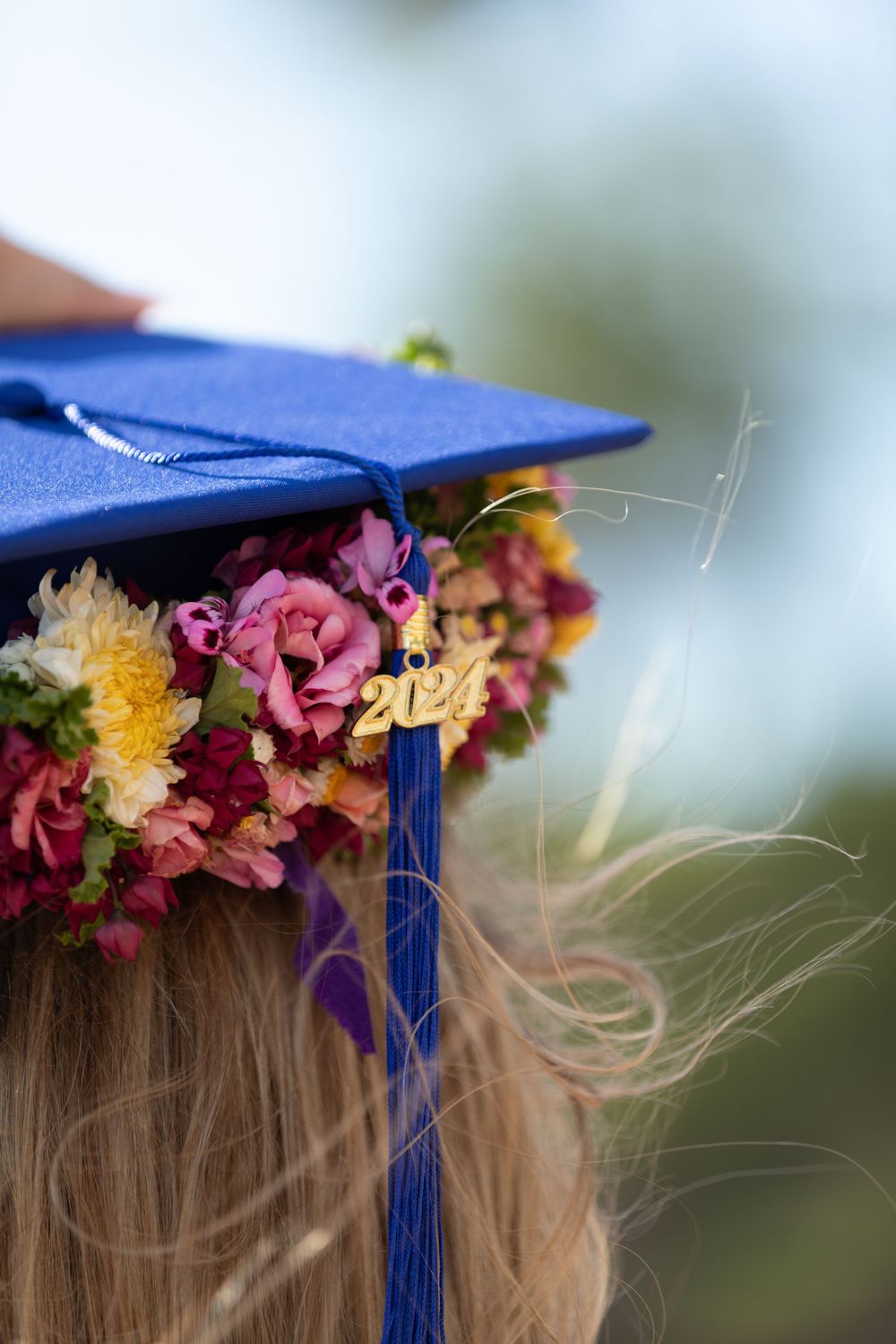 Close-up of blue graduation cap with floral crown and tassel detail.