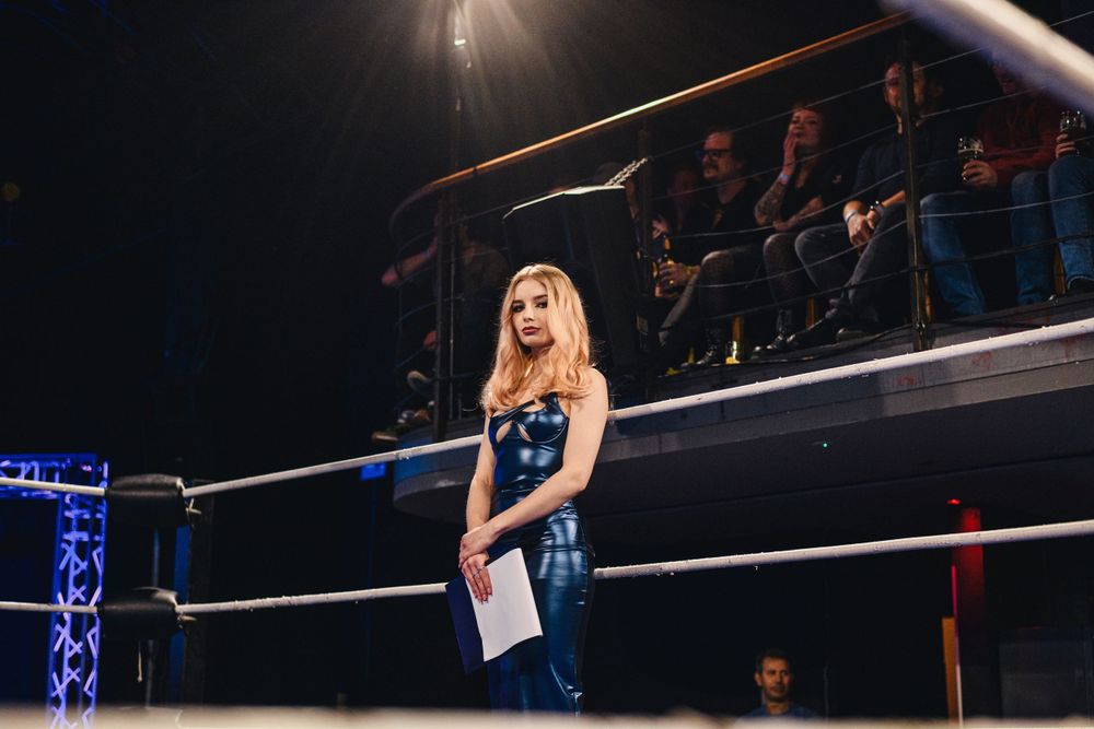 Professional wrestling match setup with dramatic lighting and metal scaffolding overhead.