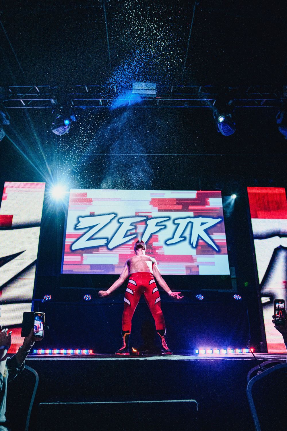 Wrestling stage production with blue lighting effects and digital screen displays.