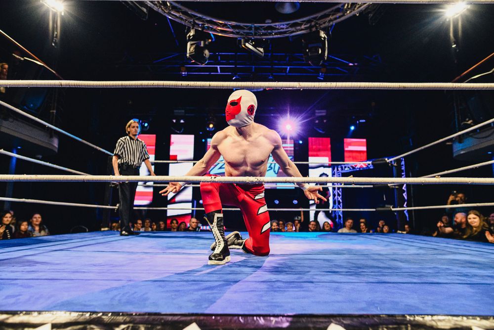 Professional wrestling match in progress with referee and ring ropes visible.