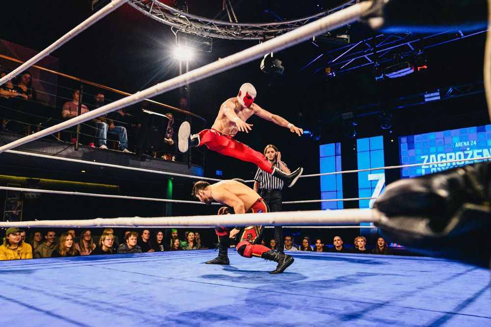 Professional wrestlers execute an impressive aerial maneuver off the top rope in a wrestling ring during a match.