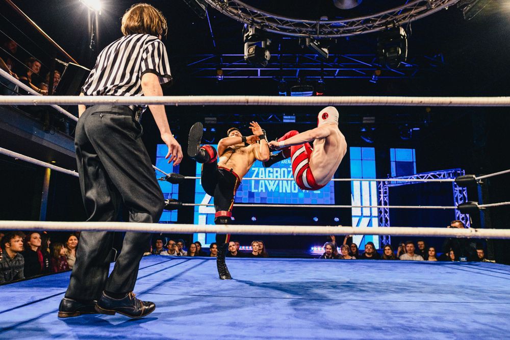 Two wrestlers engage in an athletic sequence with one performing a flying move off the top turnbuckle.
