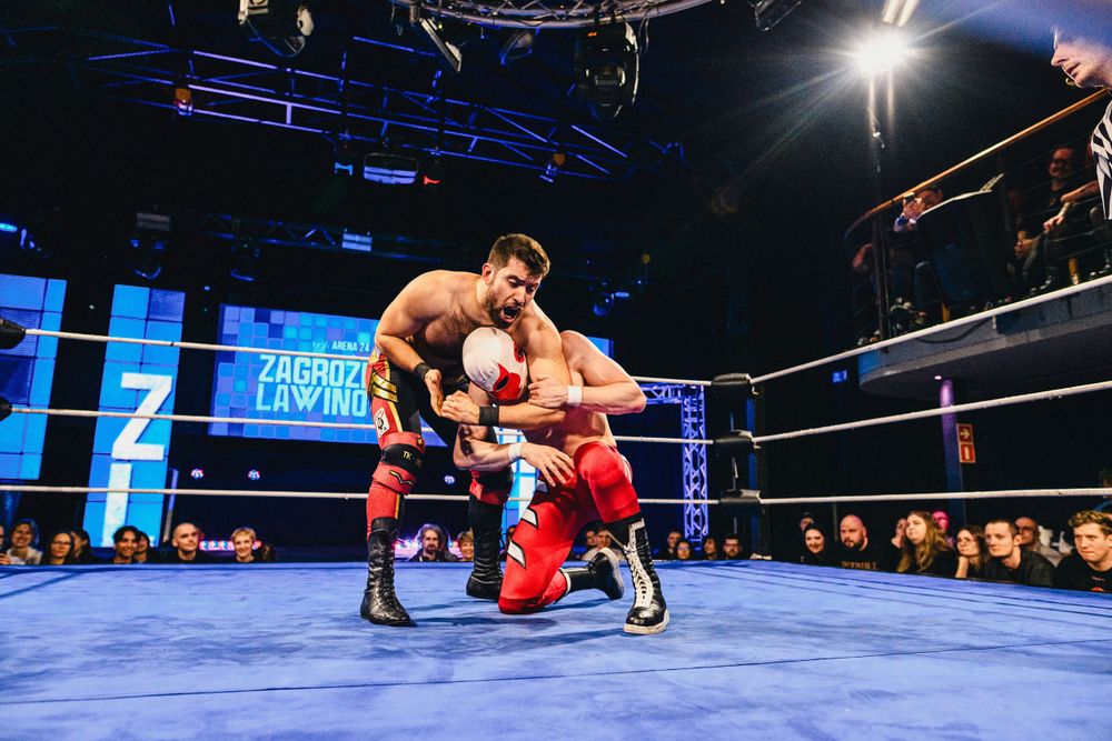 Wrestlers demonstrate their athleticism with a spectacular top rope maneuver in a brightly lit arena.