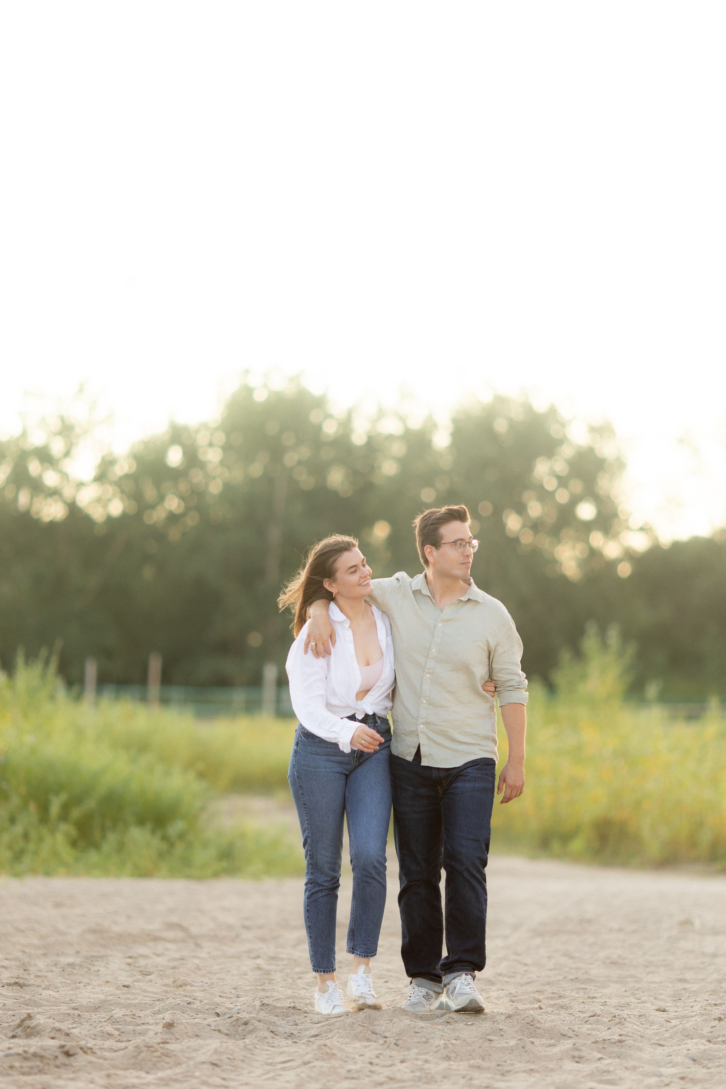 Couple strolls together on sandy path in casual attire during golden hour.