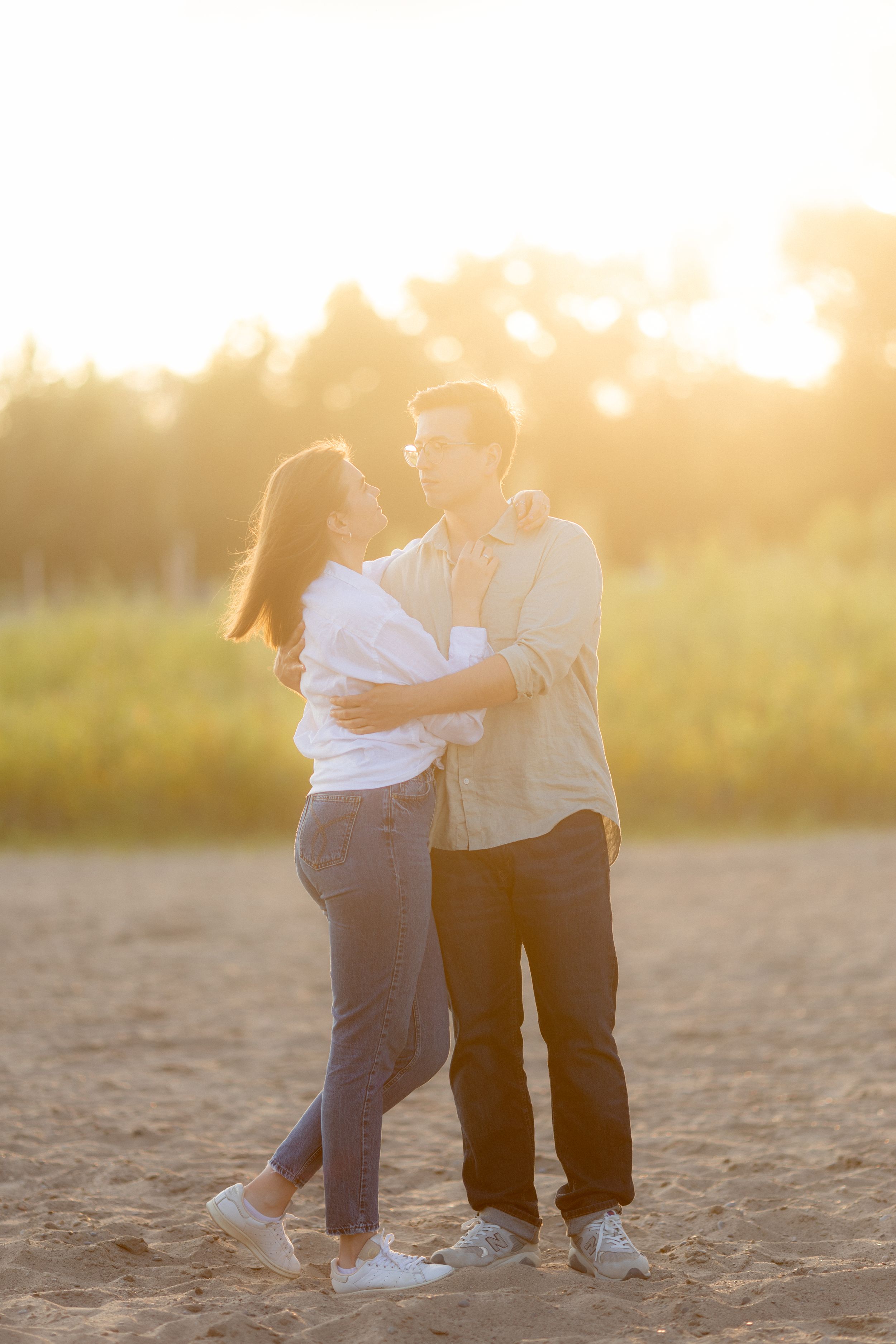 Couple embraces in golden sunset light on sandy path.