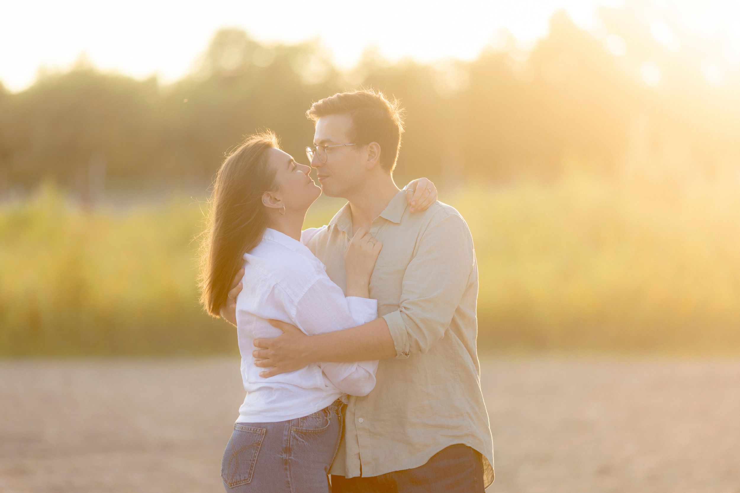 Romantic couple embraces during golden hour sunset in a field.