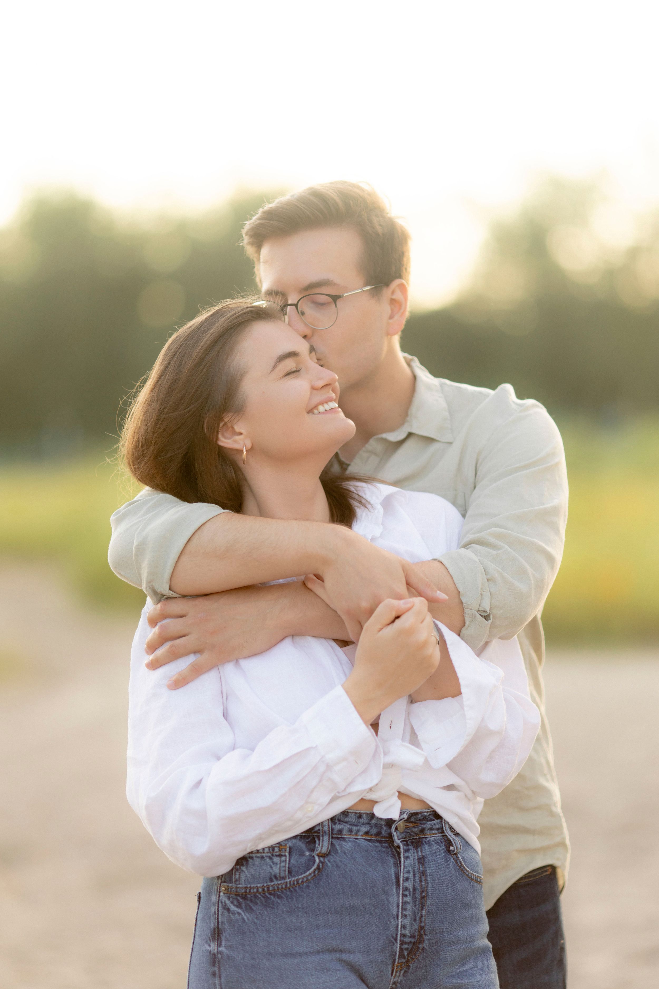Intimate embrace between couple in casual attire during sunset photoshoot.