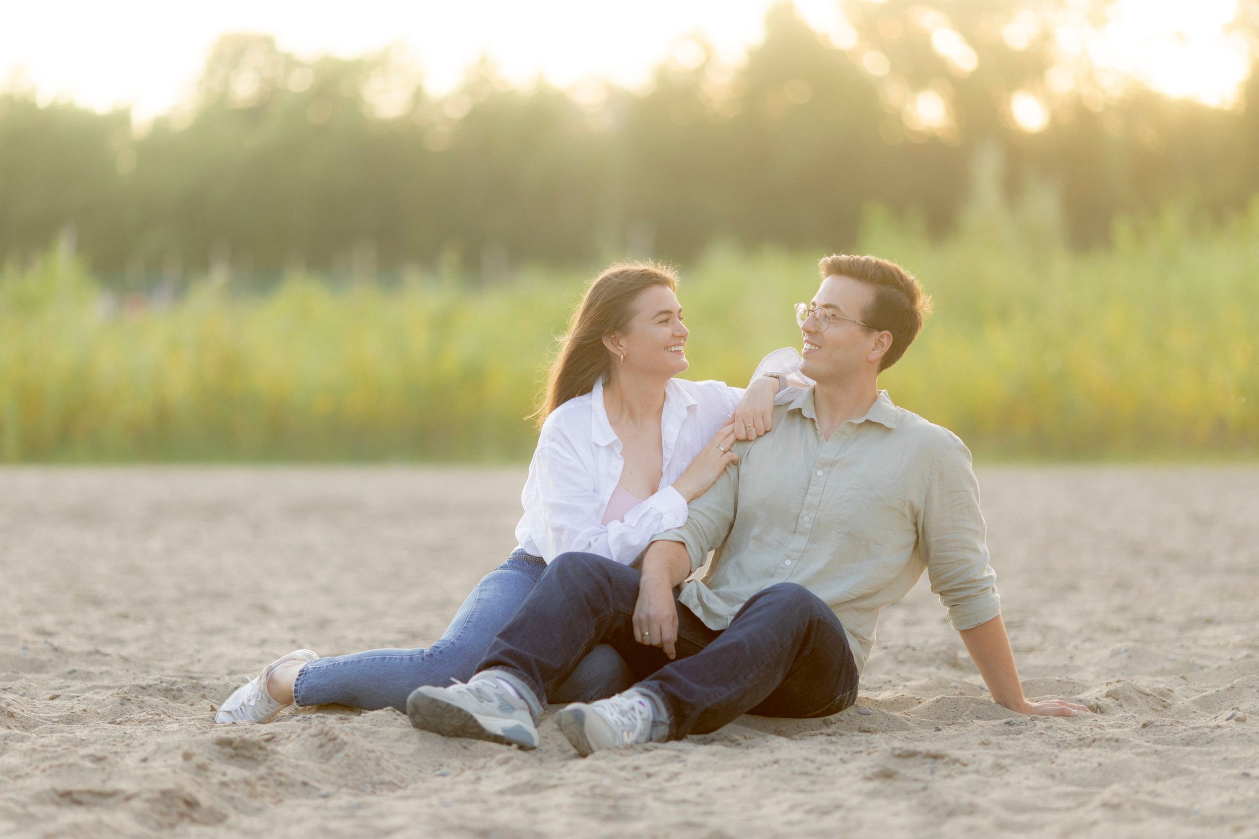 Happy couple sitting on sandy ground laughing during sunset.