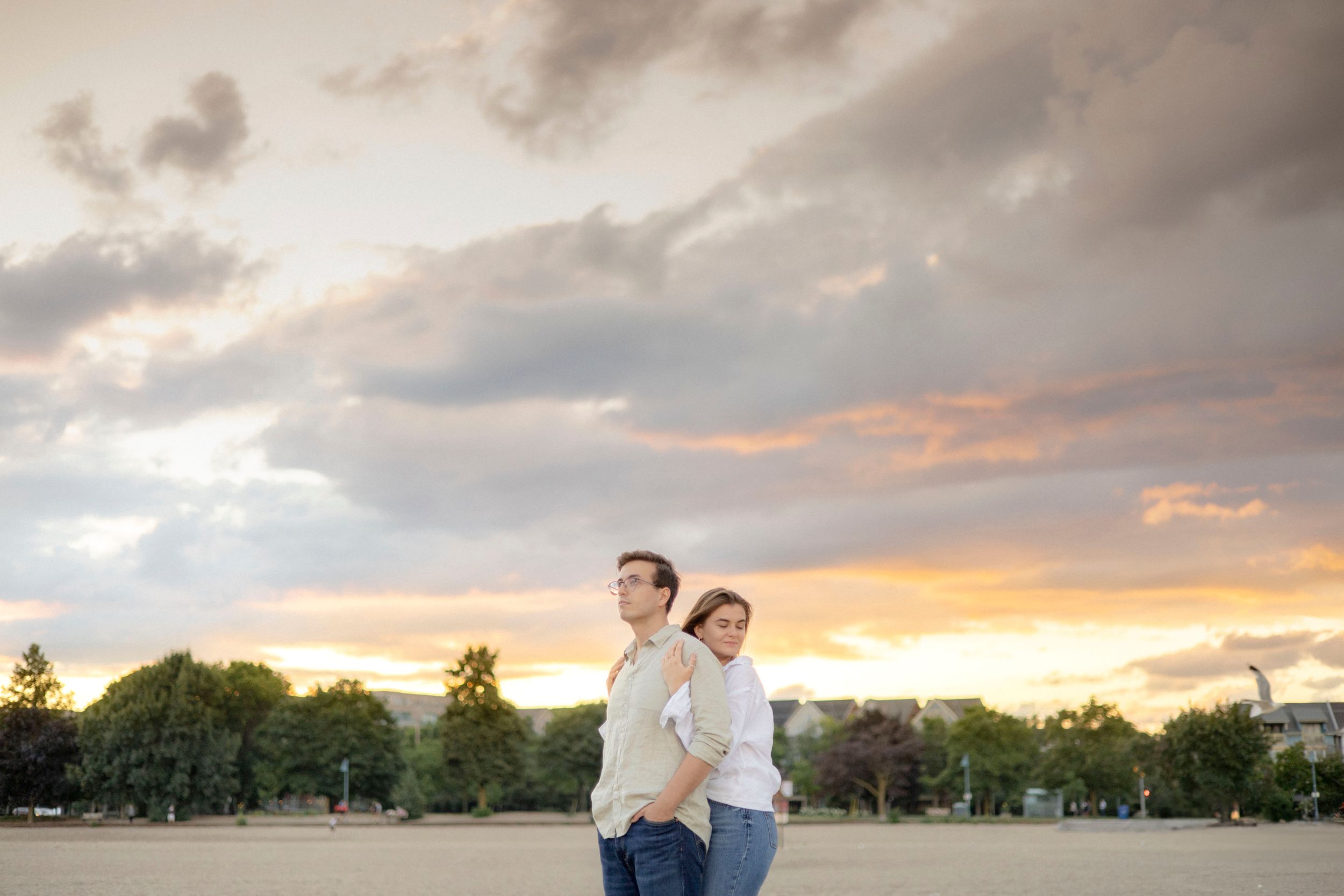 Couple standing together against cloudy sunset sky in open field.