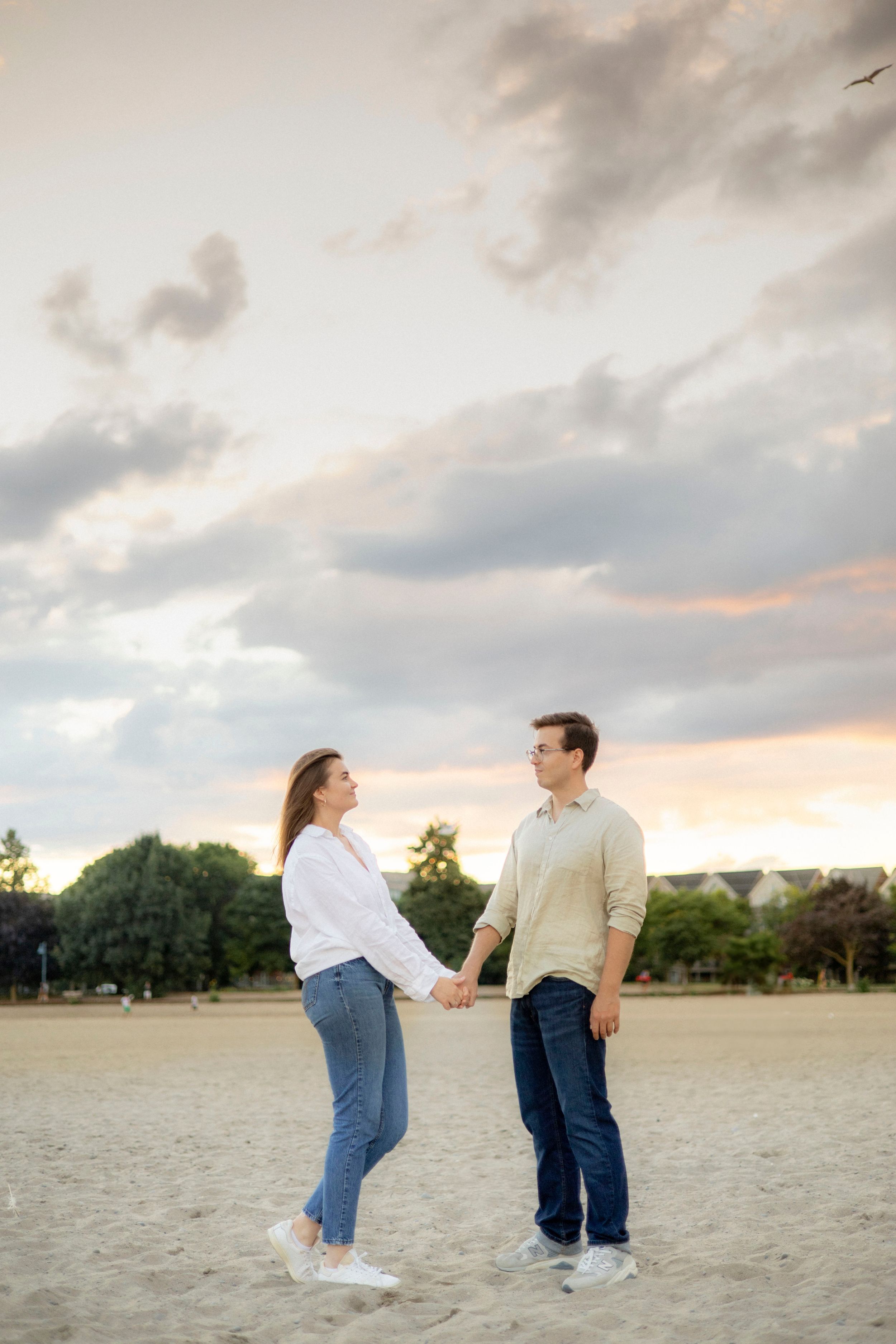 Playful couple holding hands in open field during sunset.