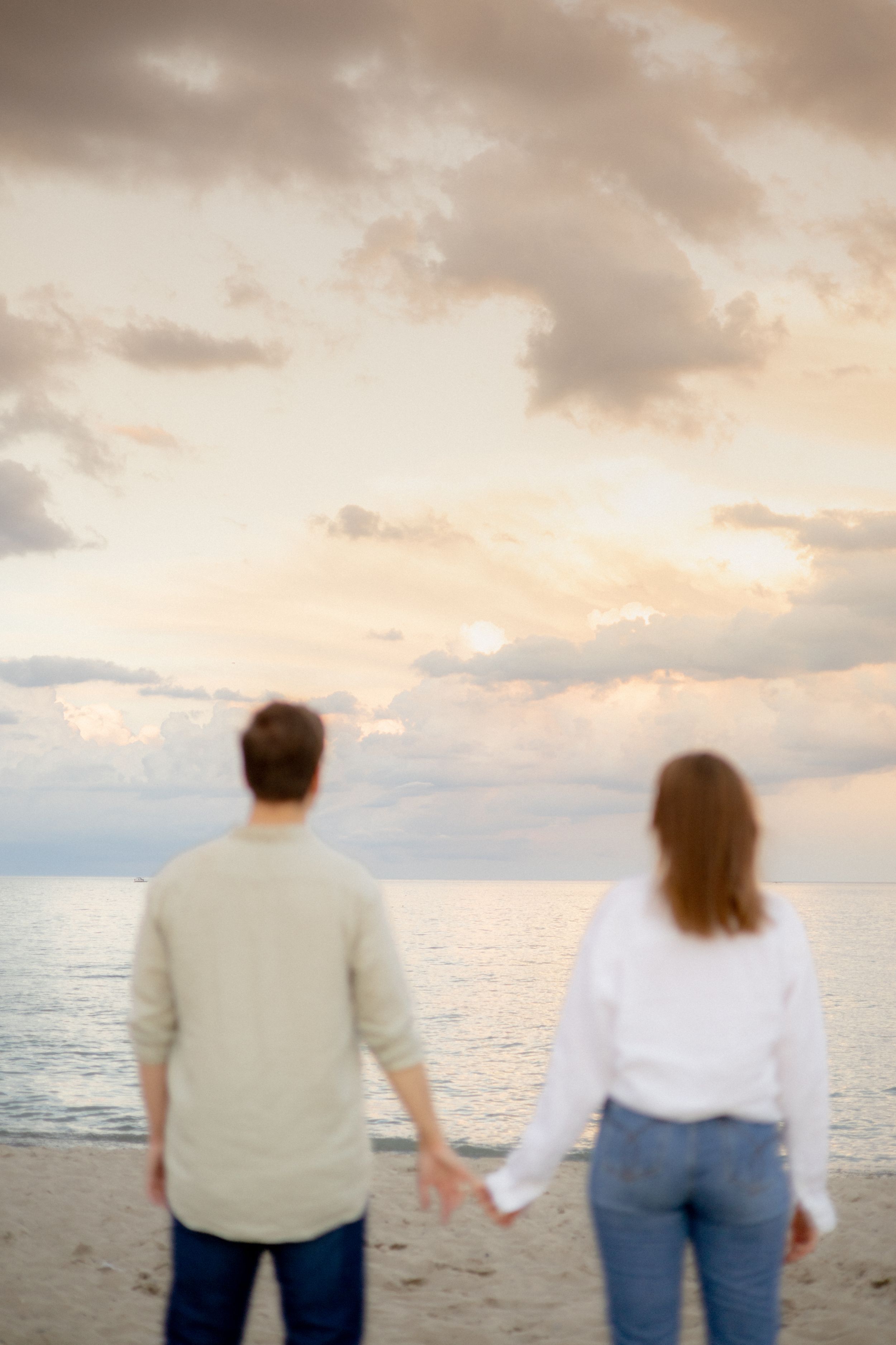 Back view of couple holding hands while watching sunset over ocean.