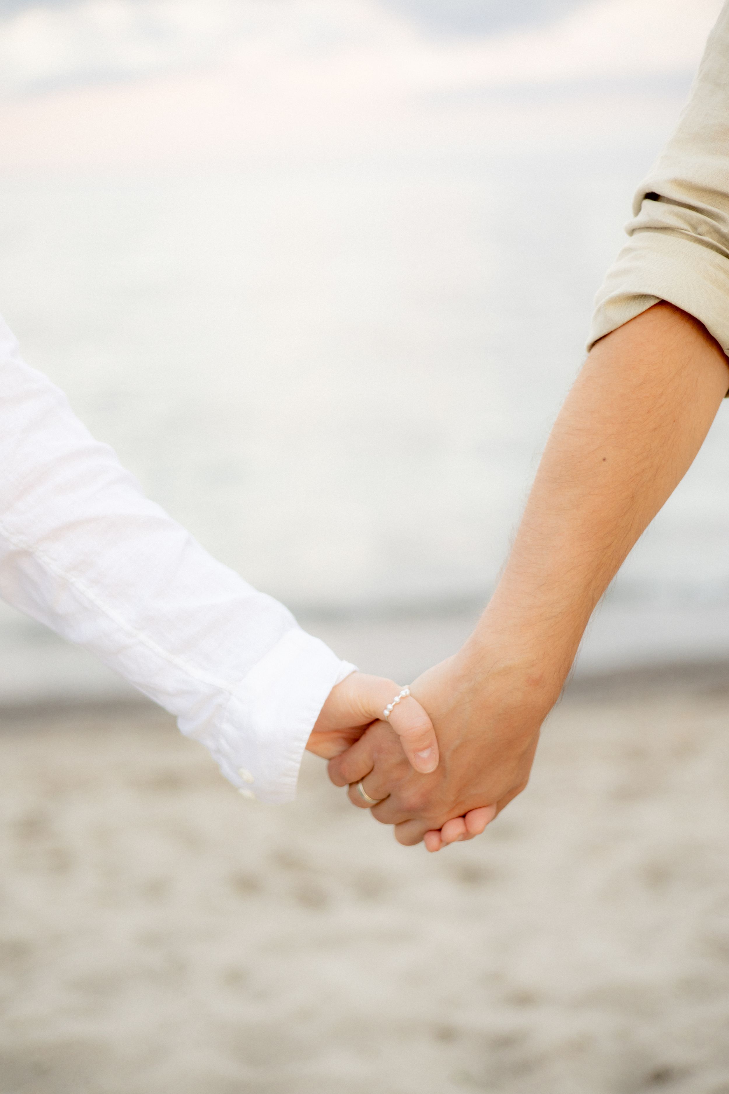 Close-up view of two people holding hands on a sandy beach.