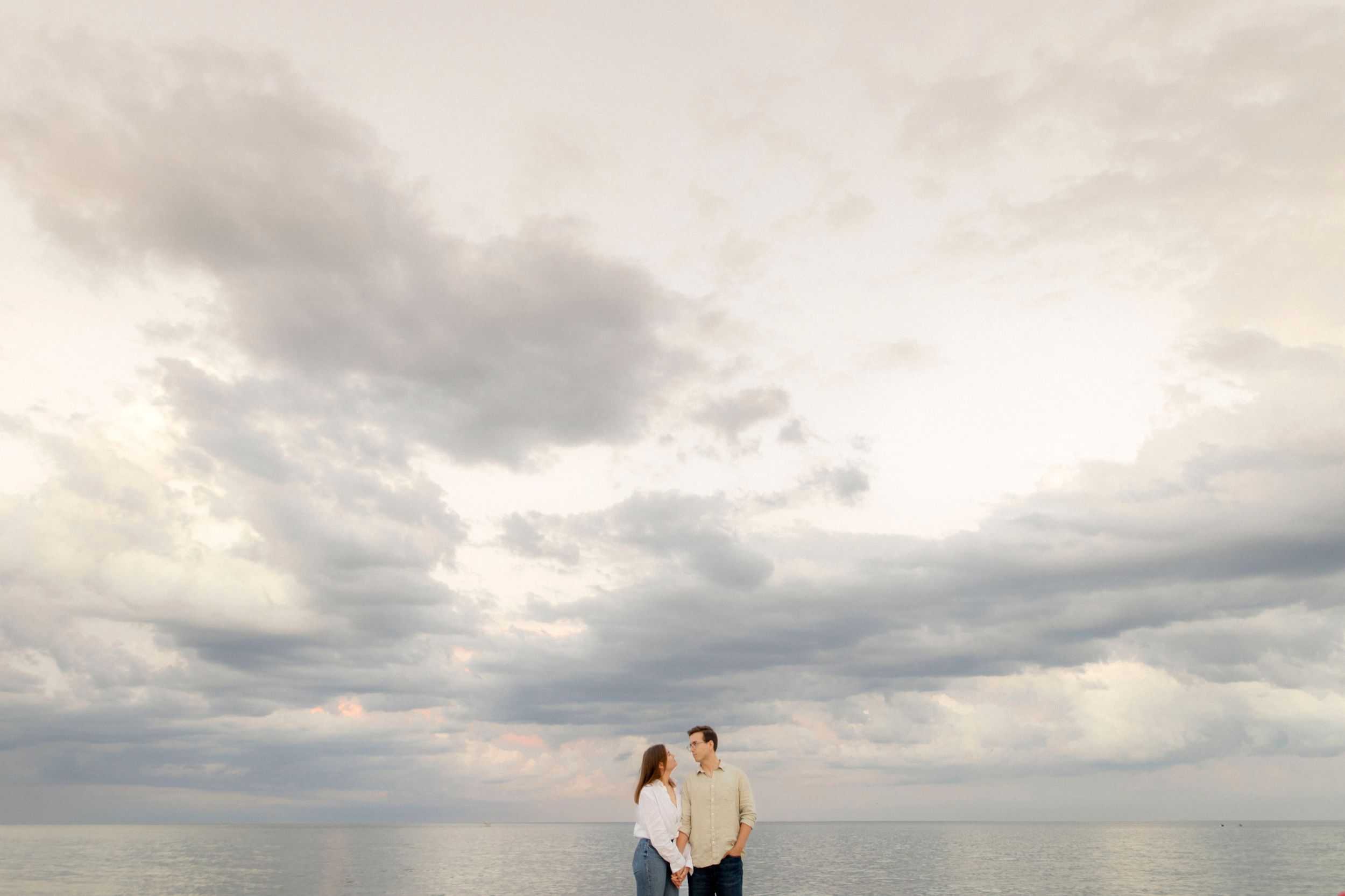 Two people stand together against a dramatic cloudy sky overlooking the ocean.
