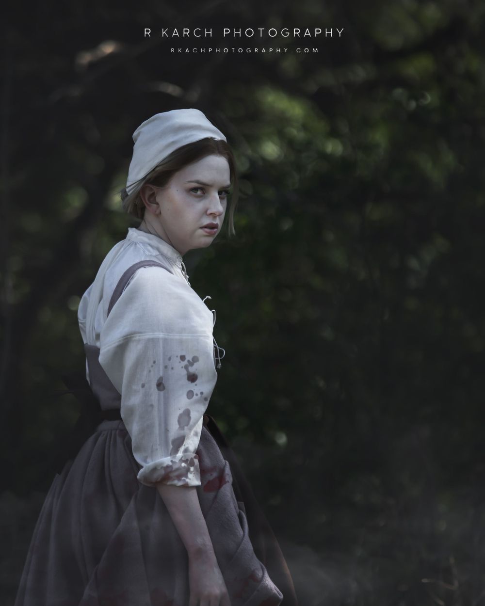 A moody portrait in historical dress features someone in a white blouse and dark skirt.
