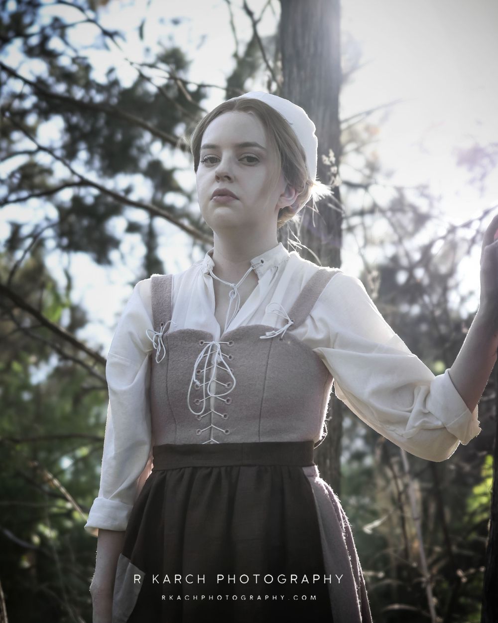 A period costume portrait shows someone in a white blouse and brown corset dress outdoors.