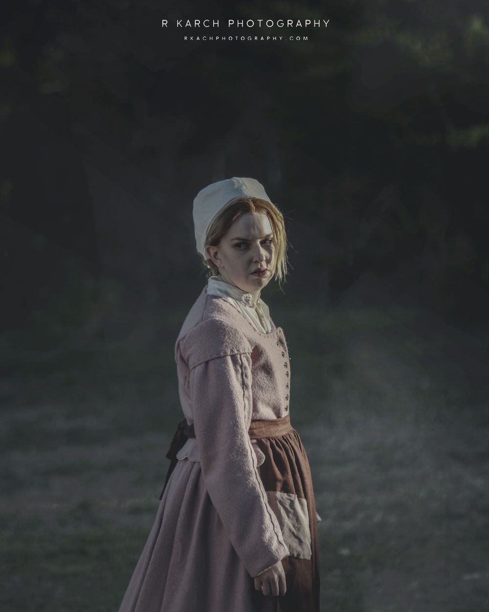 Moody portrait of person in historical peasant dress standing in misty evening light.