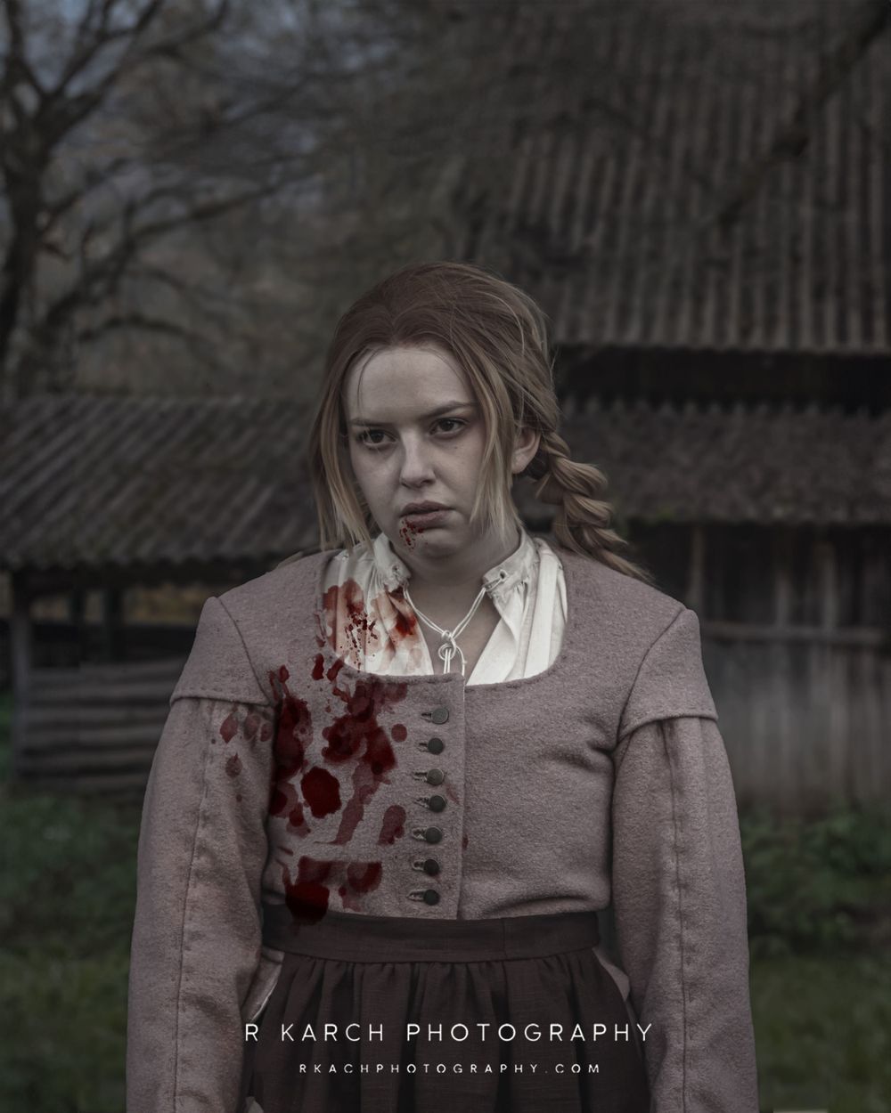 Period costume with blood-stained jacket against rustic barn backdrop in dark lighting.