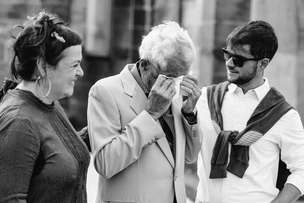 Black and white photo of wedding guests sharing emotional embraces outdoors.
