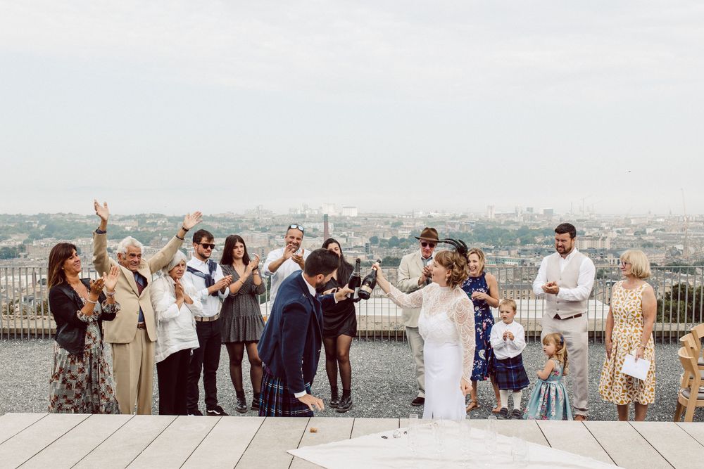 Wedding celebration on rooftop terrace overlooking historic Edinburgh cityscape.