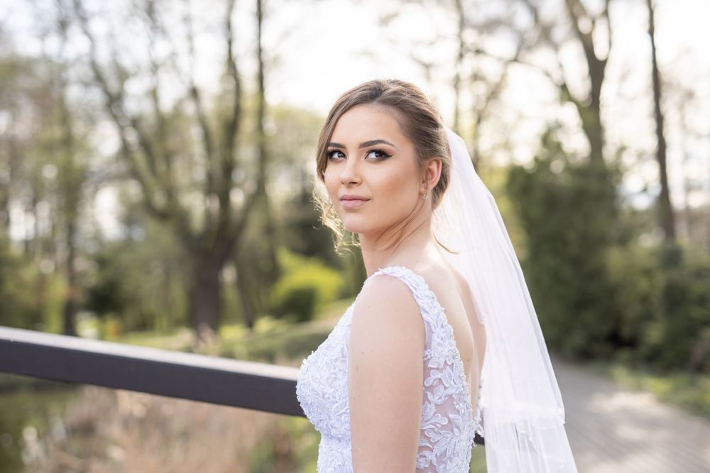 Bride in lace dress and veil looking away pensively in outdoor setting.
