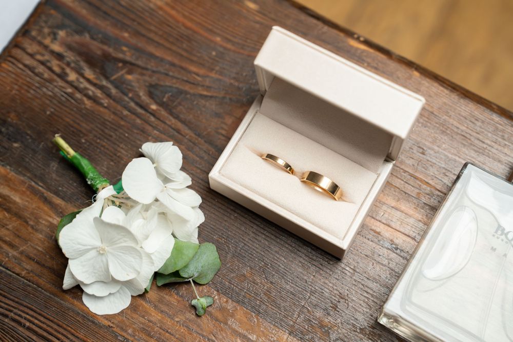 Wedding rings in white box with white orchid flowers on wooden surface.