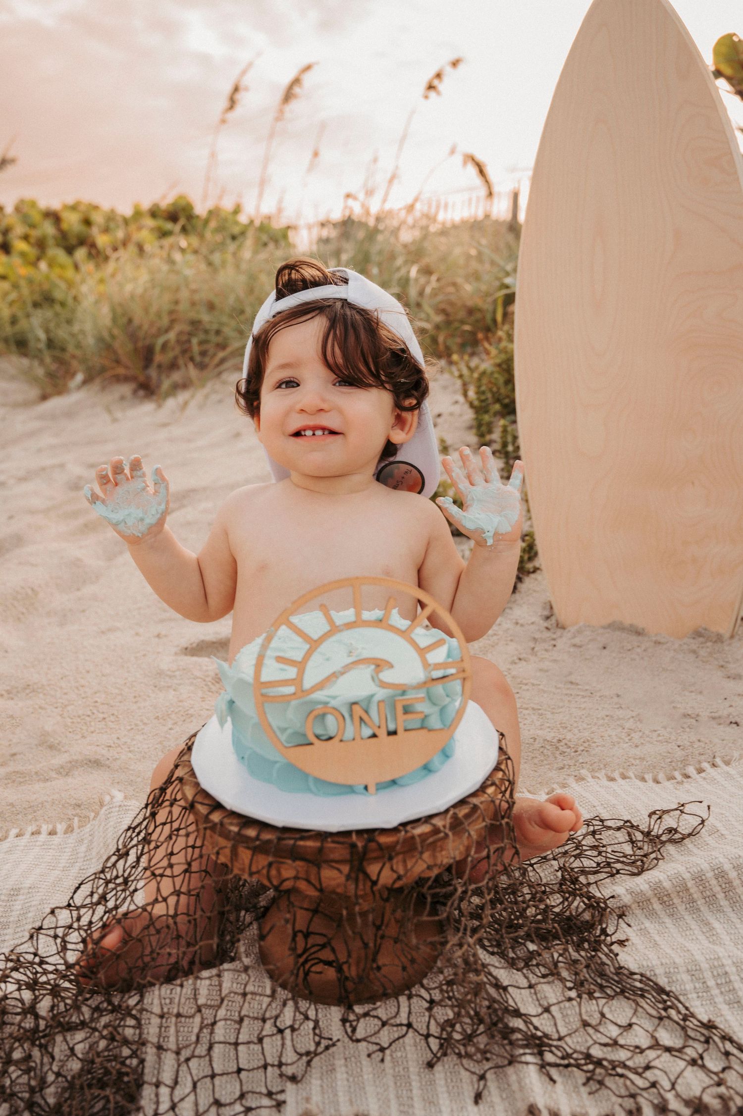 Toddler smashing a white citrus decorated first birthday cake on green grass.