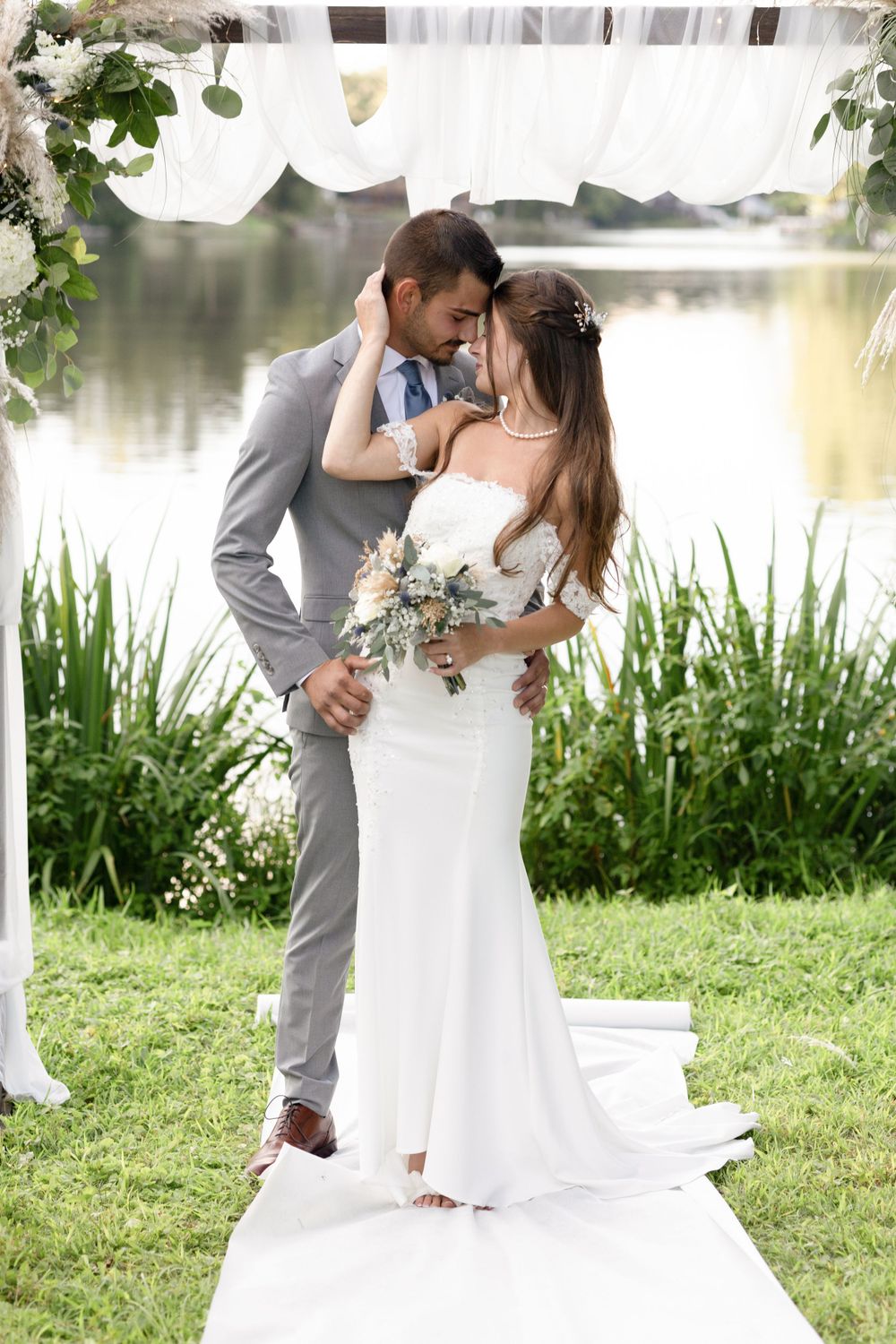 Romantic wedding couple shares intimate moment under white canopy by lakeside.