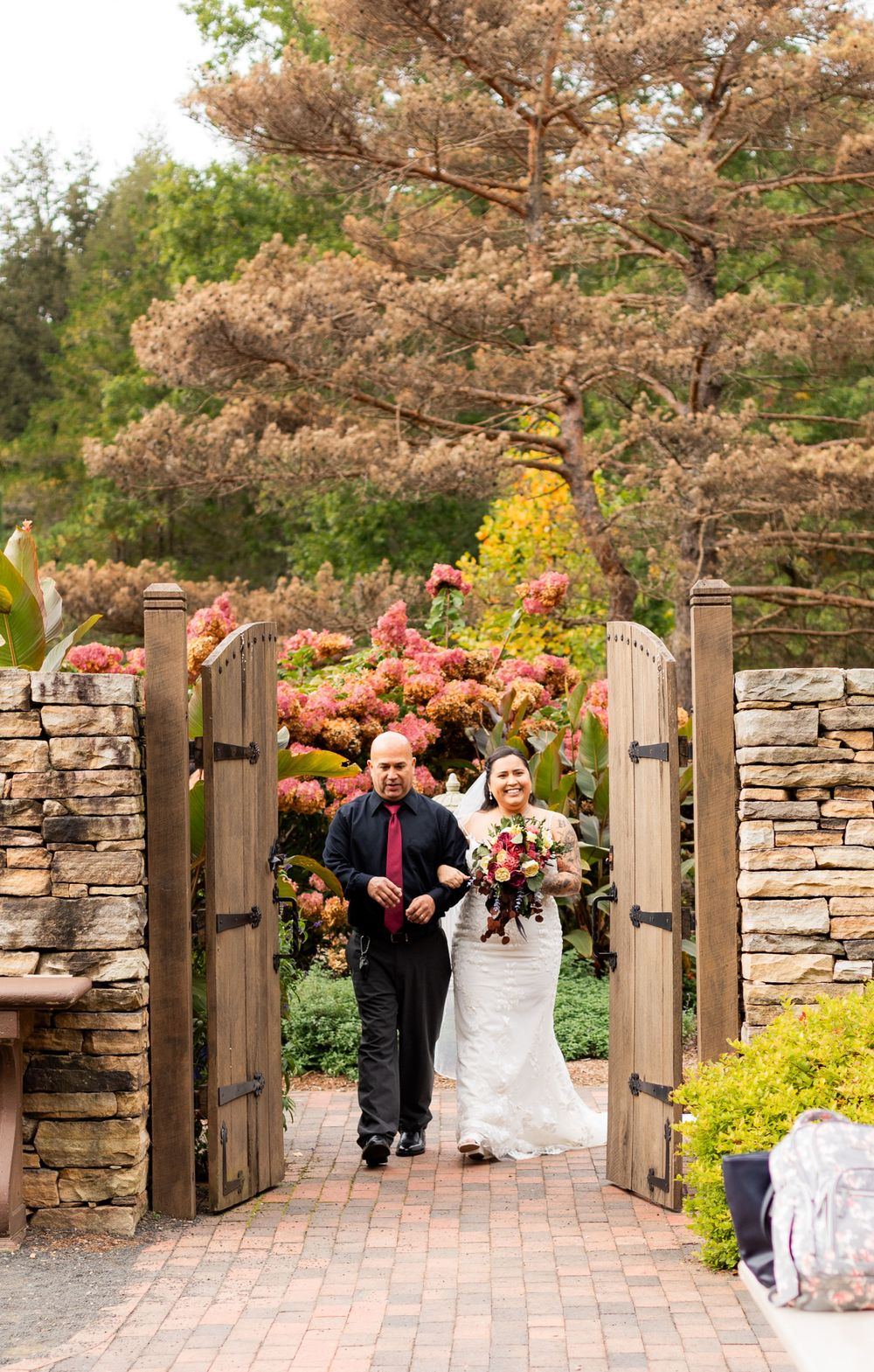 Stone wall garden entrance with wooden gates and autumn foliage.