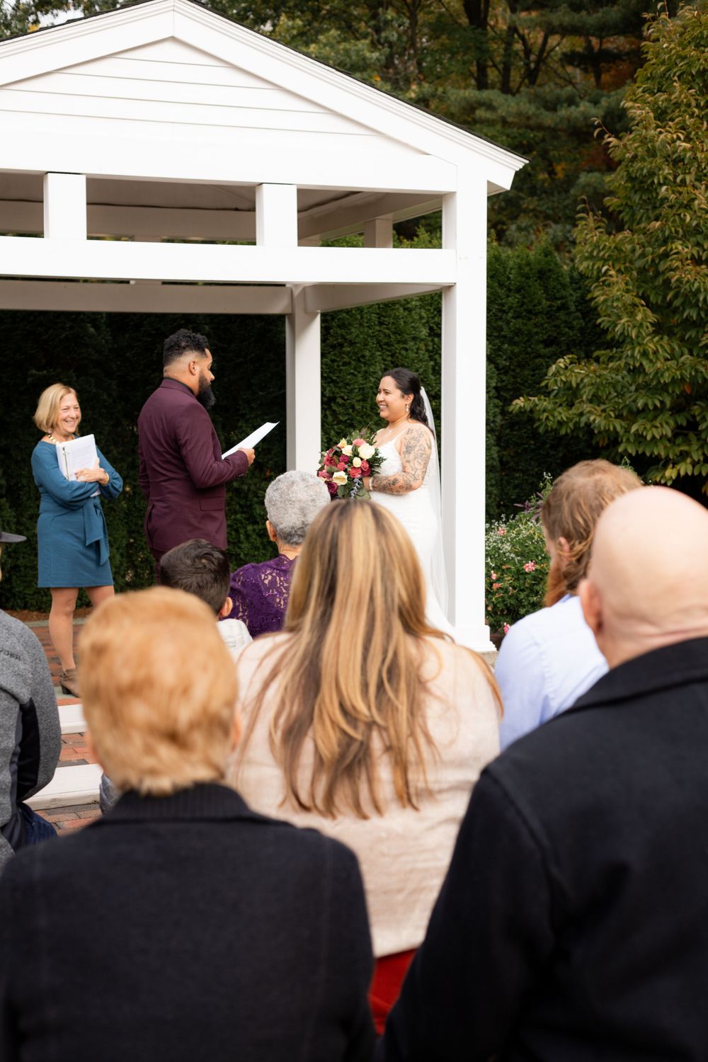 Wedding ceremony at white gazebo with guests seated outdoors.