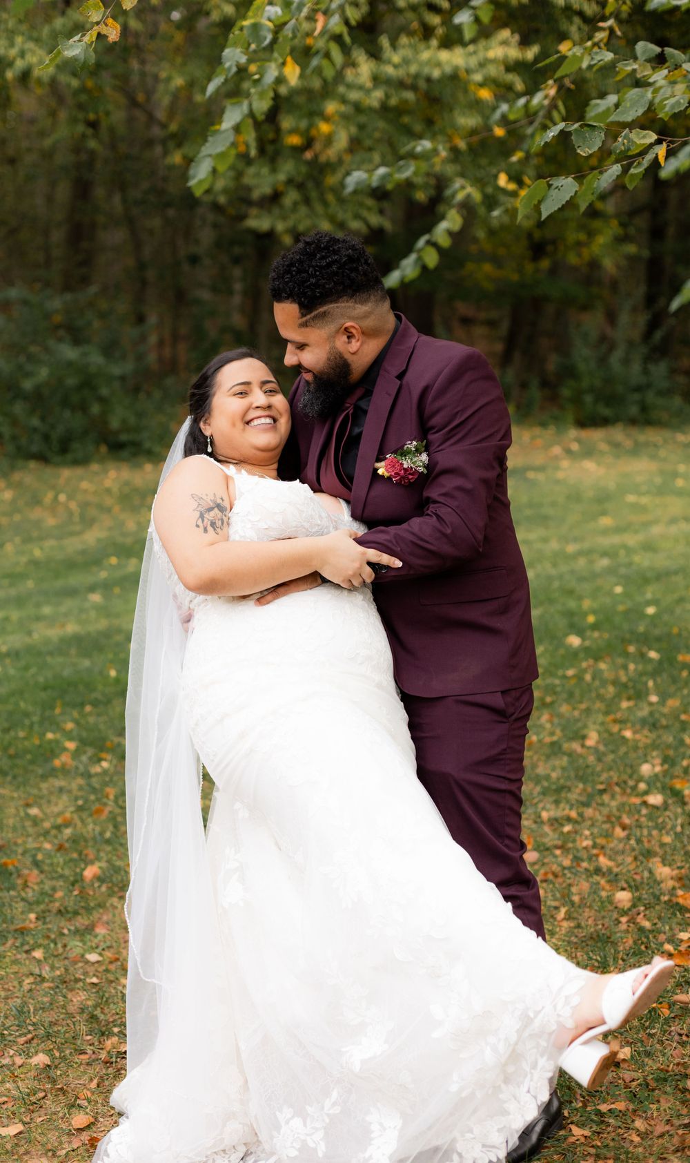 Couple in burgundy and white attire embracing in autumn garden setting.