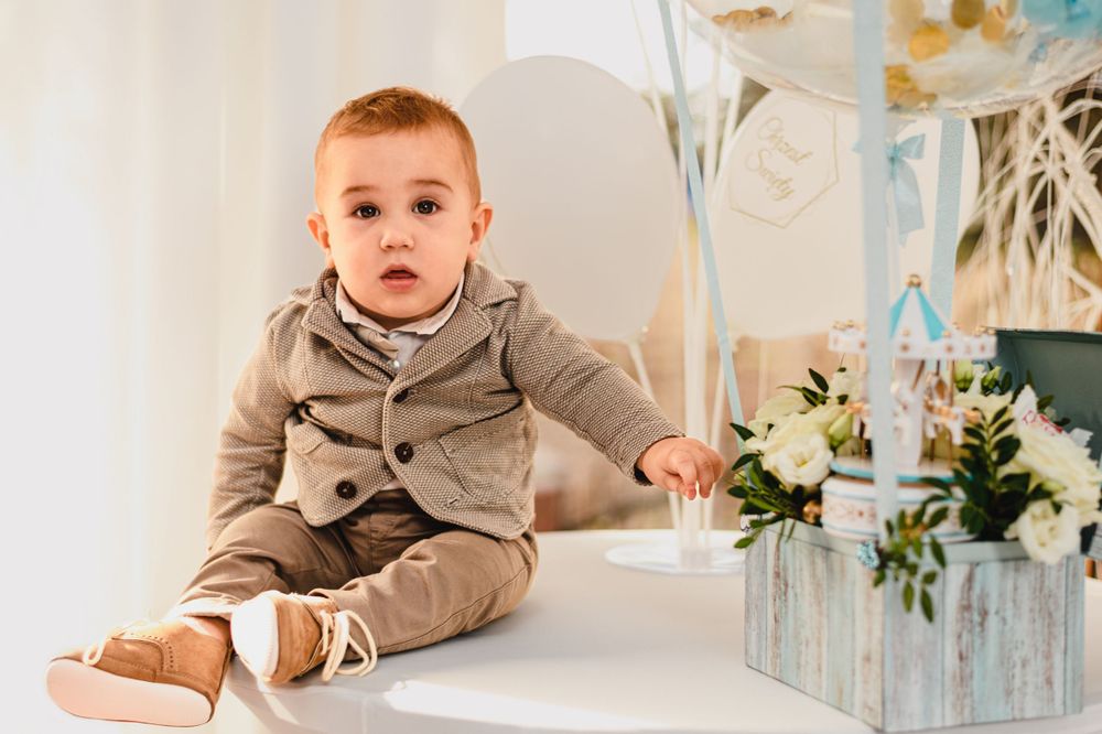 Baby in a beige formal outfit posing near elegant party decorations.